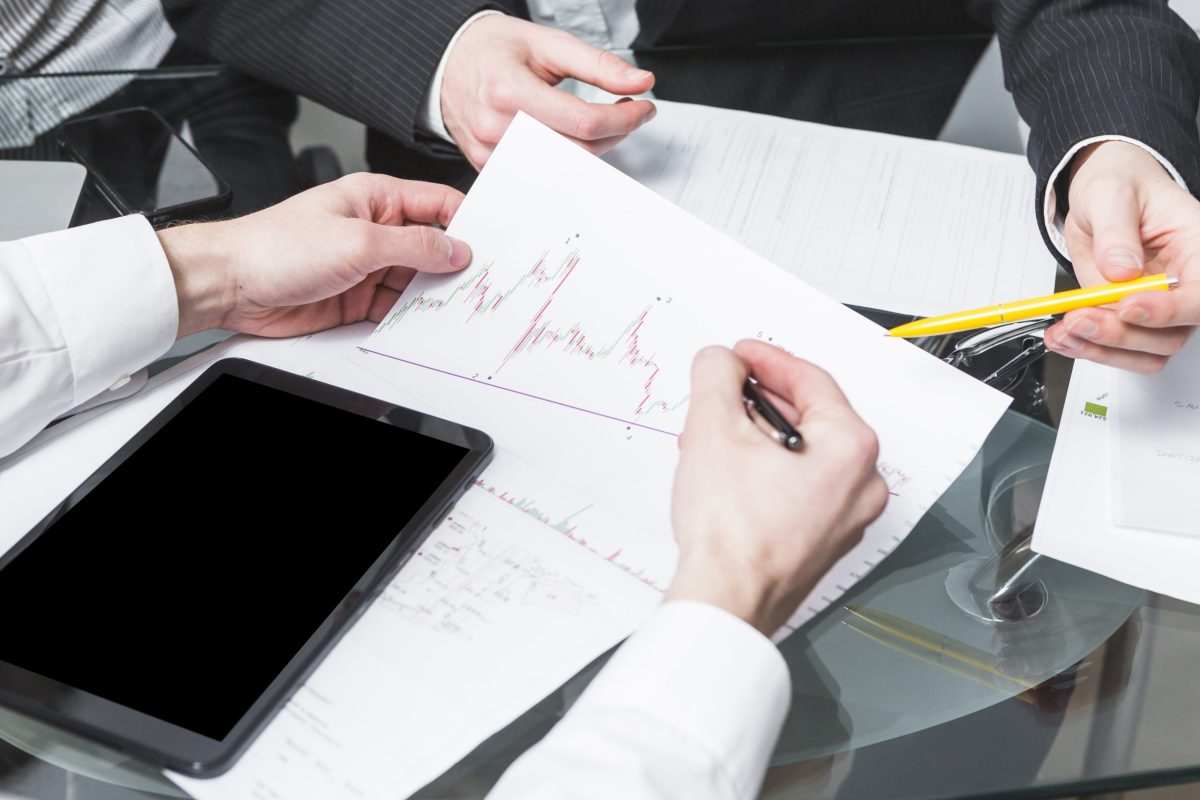 Two businesspeople in an office setting are analyzing a financial report with a candlestick chart, a key skill for passing a free prop firm challenge.